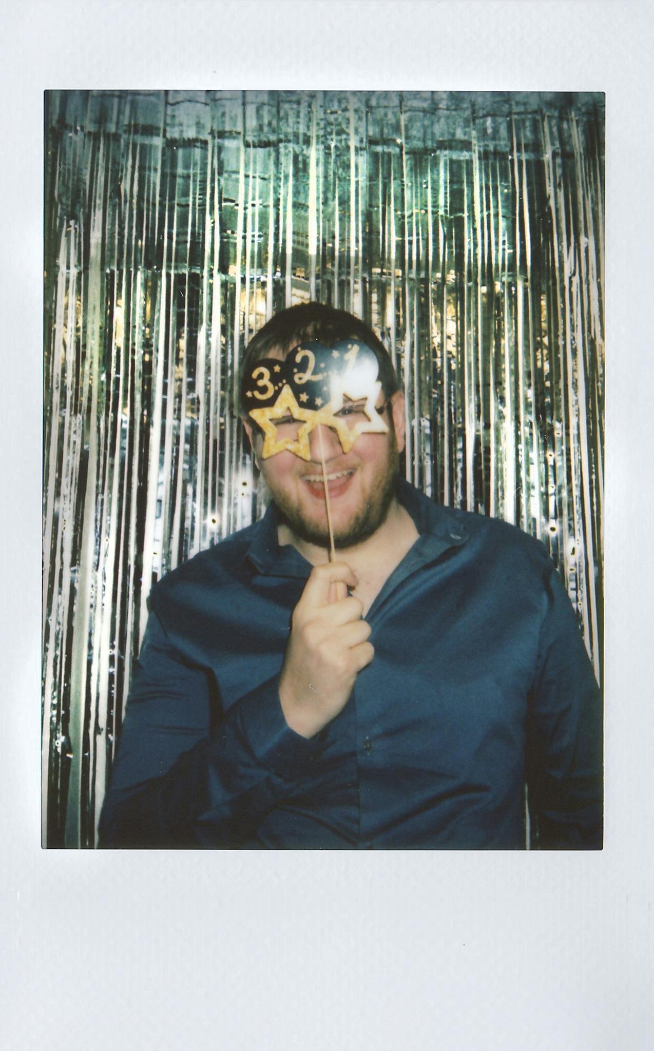 Man celebrating with '30' prop in front of shimmering backdrop, holding a playful expression.